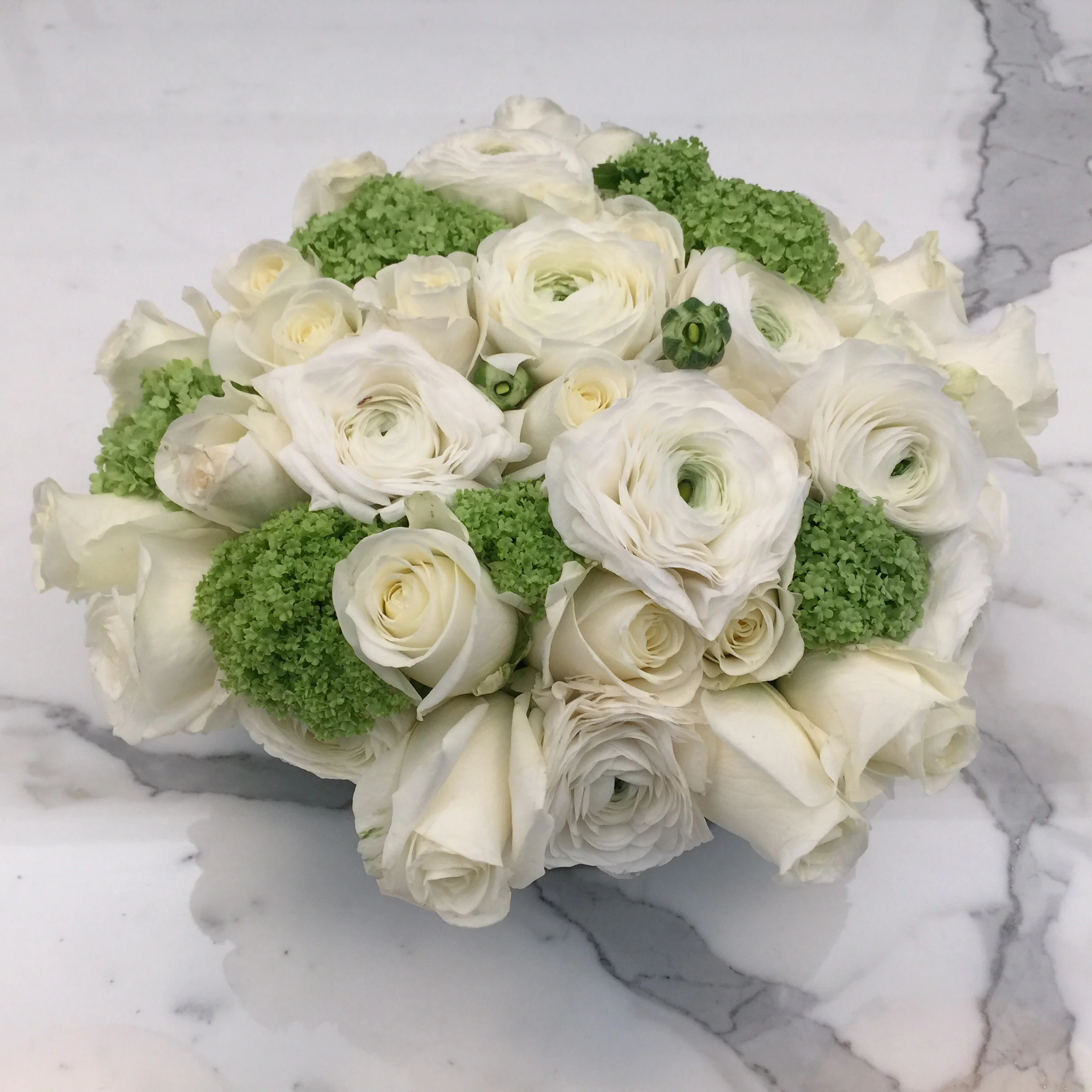 White ranunculus and viburnum arranged on marble